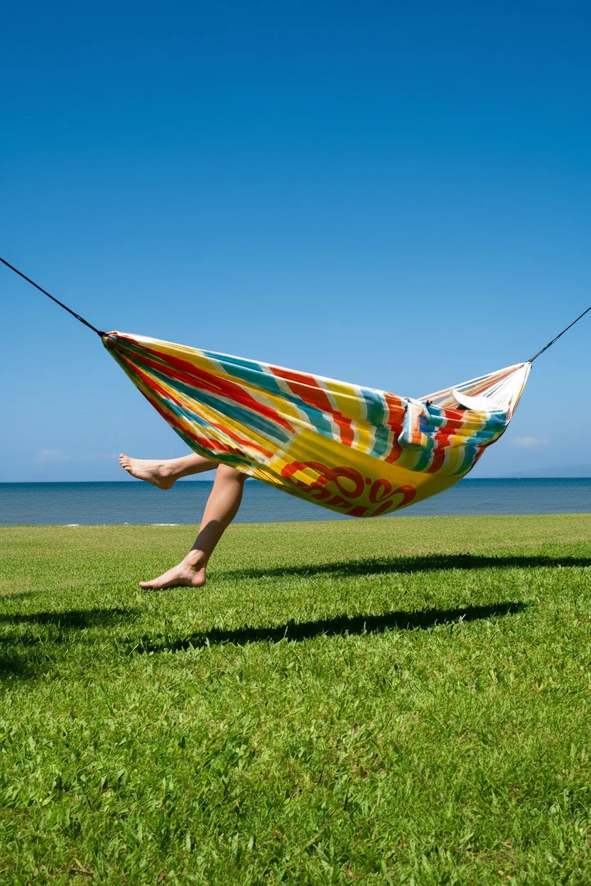 Person relaxing in a colorful striped hammock on a grassy area with a clear blue sky.