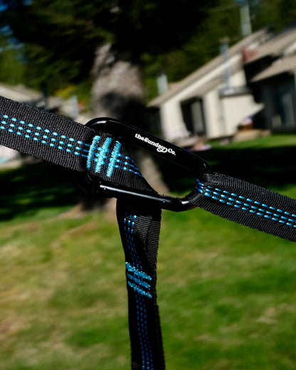 The Sunday Company close-up of the Sunburst black and blue strap with a logo carabiner in a backyard