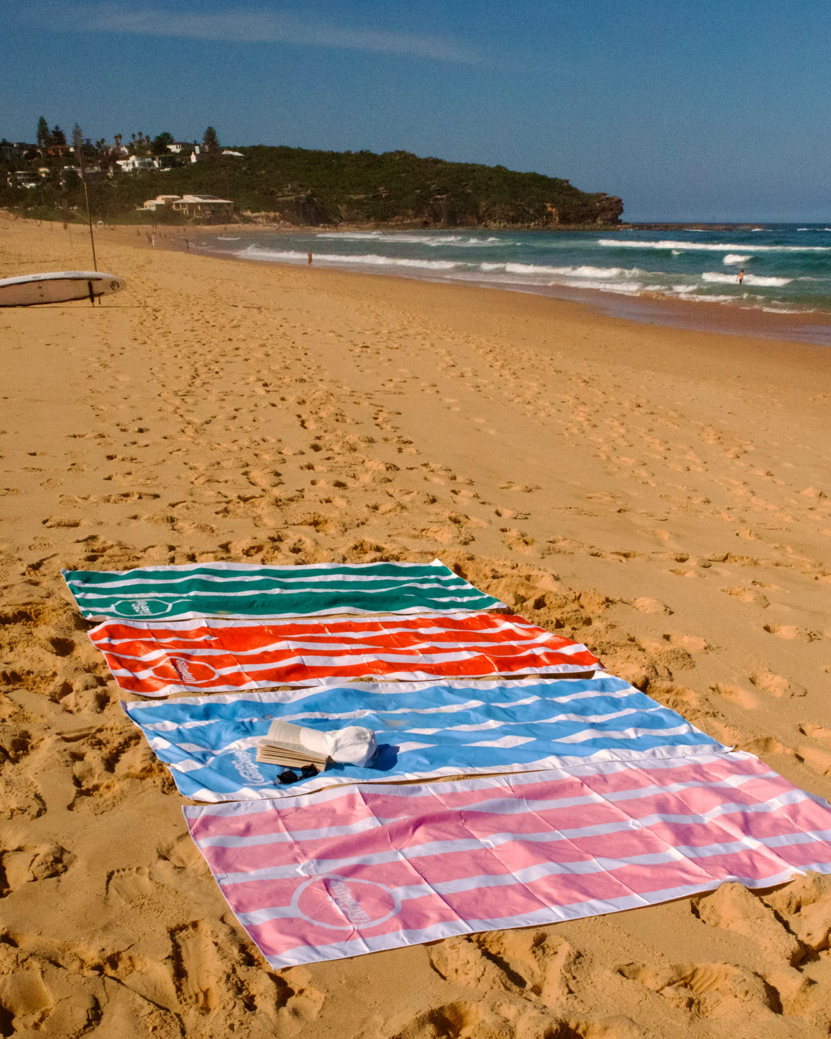 Colorful towels on a sandy beach with ocean and cliffs in the background
