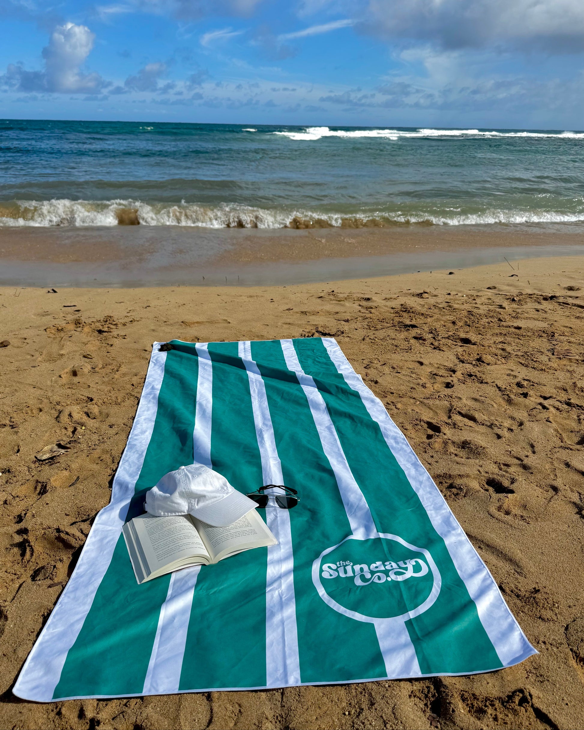 Green and white striped towel on a sandy beach with ocean waves in the background