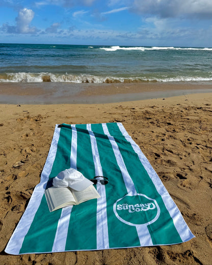 Green and white striped towel on a sandy beach with ocean waves in the background