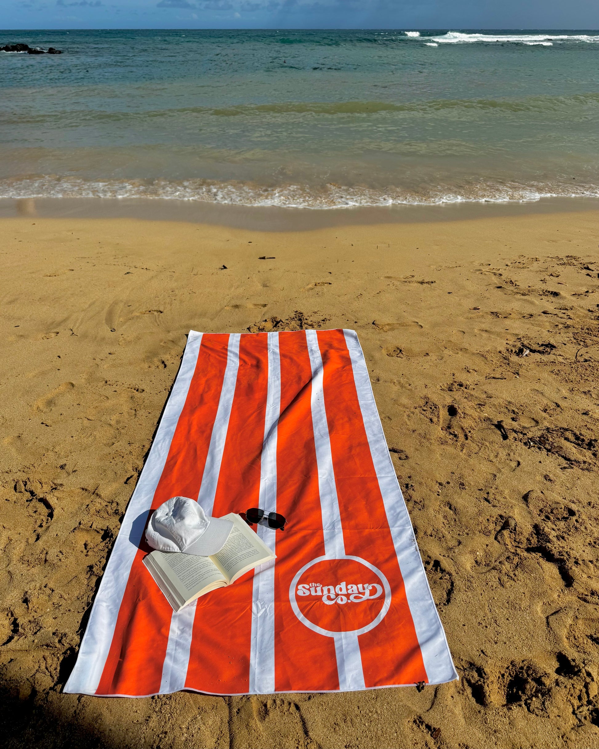 Orange and white striped towel on a sandy beach with ocean waves in the background