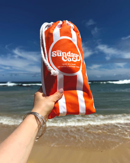 Orange and white bag with 'The Sunday Cook' logo held by a hand on a beach.